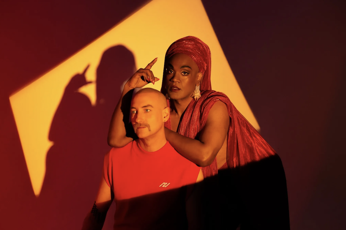 Australian electronic duo Electric Fields posing together in dramatic red and yellow lighting for a promotional studio portrait shoot.
